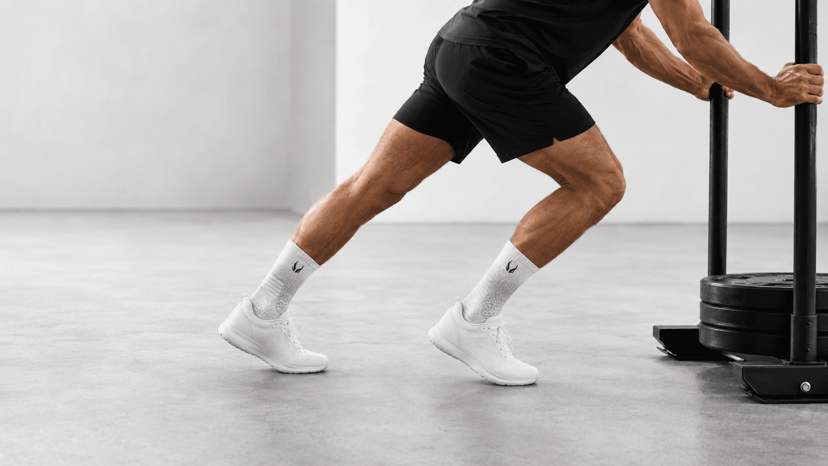 Male athlete pushing a sled during hybrid training — HOOF performance socks with gold logo visible