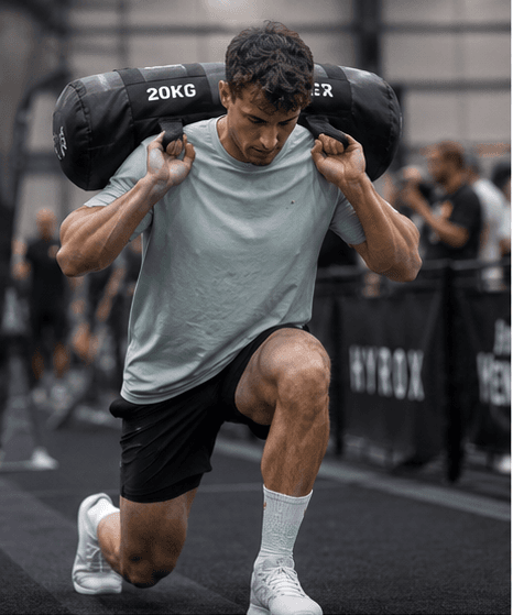 Male athlete in sandbag lunge during HYROX training — HOOF socks with gold logo